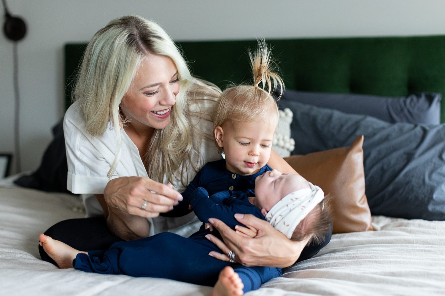 mom sitting on bed with toddler daughter and newborn baby girl