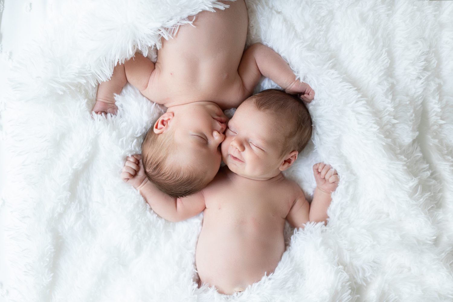 twin newborn girls snuggled together on a furry blanket