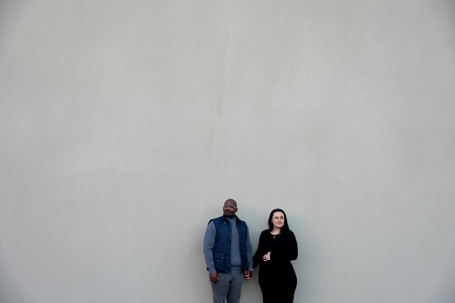 Modern maternity photo of expecting parents against simple wall