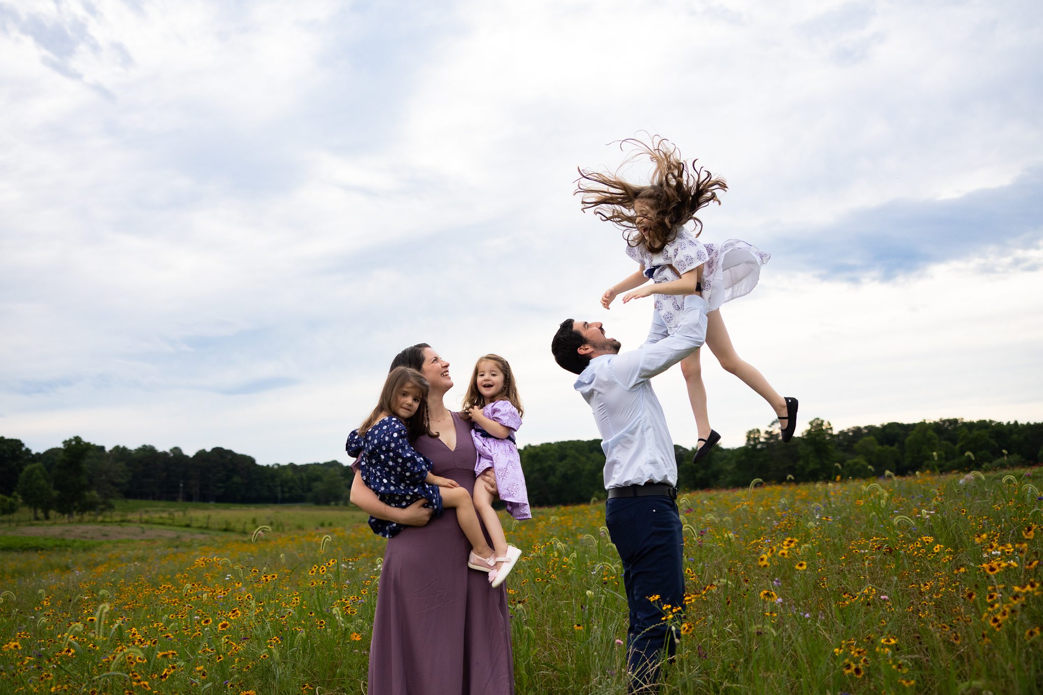 Dad tossing daughter into sky with Mom and sisters watching