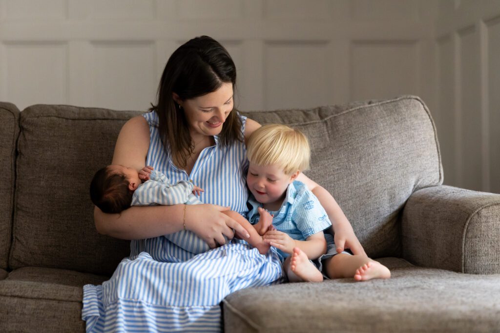 Mom holding newborn baby while toddler brother sits beside her